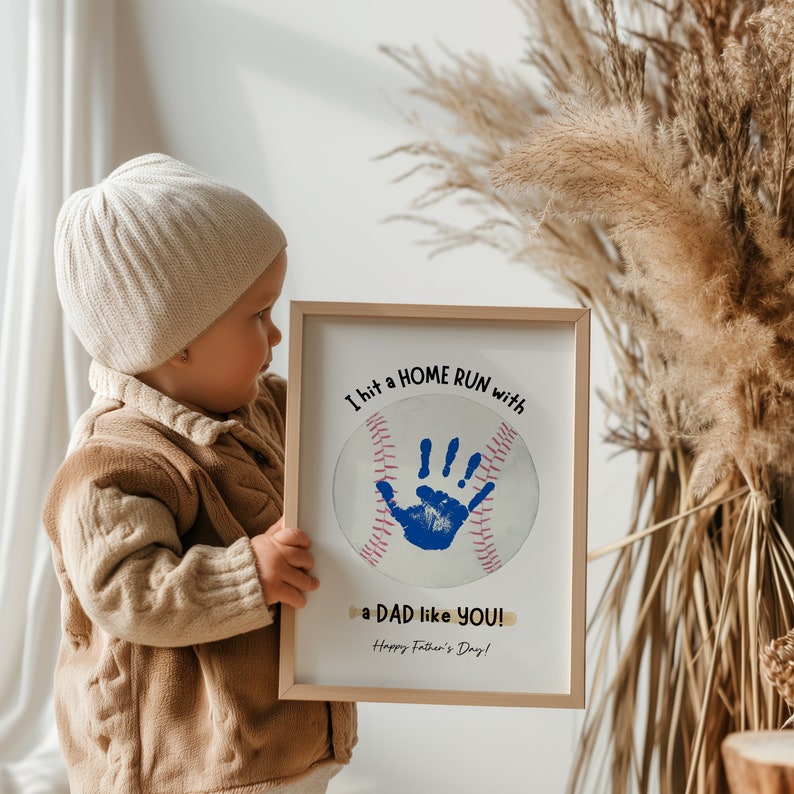 May include: A white framed print with a blue handprint inside a baseball graphic. The text reads "I hit a HOME RUN with a DAD like YOU! Happy Father's Day!"