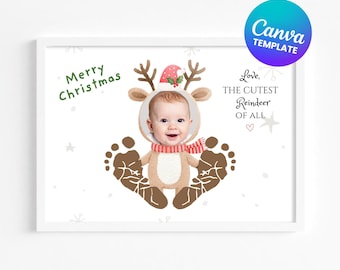 May include: A framed print with a baby dressed as a reindeer, wearing a red and white striped scarf and hat. The words "Merry Christmas" are in green, and "Love, The Cutest Reindeer Of All" is in black. Footprints are at the bottom.