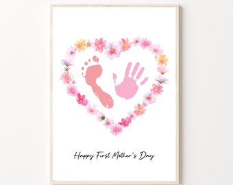 May include: A white card with a pink handprint and footprint inside a heart-shaped wreath of pink and yellow flowers. The text "Happy First Mother's Day" is printed below the hand and footprint.