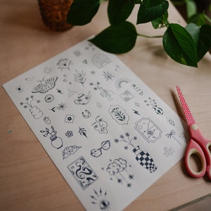 May include: A sheet of temporary tattoos with various black line art designs, including a butterfly, flowers, and clouds. The word "MISD" is visible. A pair of red and white polka dot scissors is on the right.