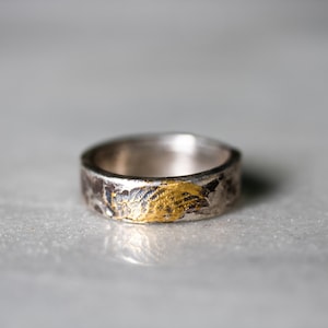 May include: A silver ring with a textured surface and a gold accent. The ring is a simple design with a subtle touch of gold.
