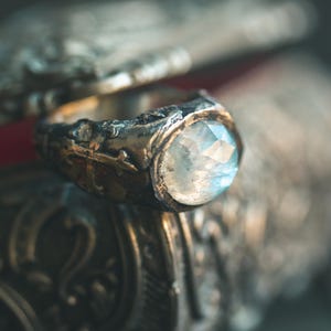 May include: A silver ring with a large, faceted, light blue gemstone set in a bezel setting. The ring is ornate and has a detailed design.
