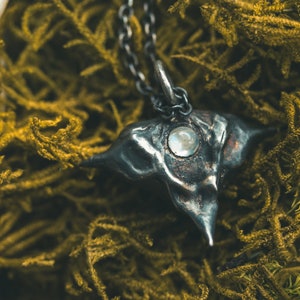 May include: A silver necklace with a unique, textured pendant shaped like a water chestnut. The pendant features a clear, iridescent gemstone in the center.