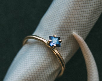Puede incluir: Un anillo de oro con una piedra preciosa azul cuadrada en el centro.