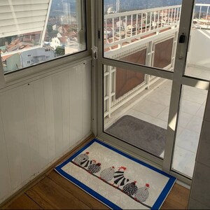 May include: A white door with a blue and white patterned doormat featuring a line of black and white chickens. The doormat is on a wooden floor.