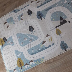 Puede incluir: Una alfombra de juego blanca con un dise&ntilde;o de carretera azul. La carretera tiene varias ilustraciones de animales y naturaleza, incluyendo &aacute;rboles, p&aacute;jaros y monta&ntilde;as.