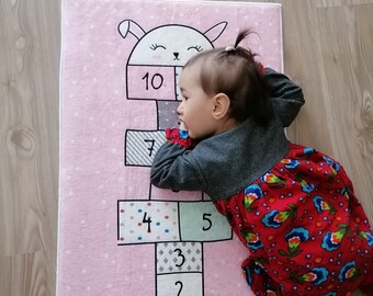 May include: A pink play mat with a white bunny design and numbers 1 through 10. A young child is lying on the mat.
