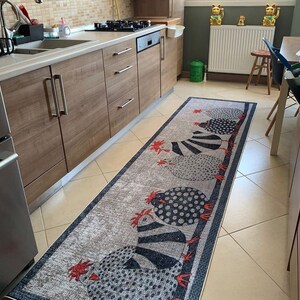May include: A long, rectangular, gray and white kitchen rug with a black and white chicken design. The rug has a black border with a white stripe.