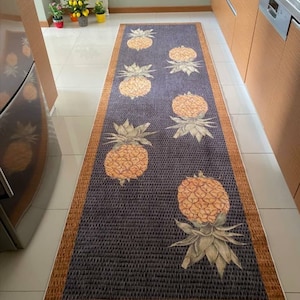 May include: A kitchen rug with a dark gray background and a brown border. The rug features a repeating pattern of yellow pineapples with green leaves.