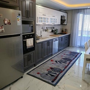 May include: A modern kitchen with dark gray cabinets, white cabinets with glass doors, stainless steel appliances, and a white tiled backsplash. A blue and white rug with a red rooster design is on the floor.
