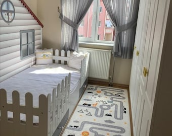 Puede incluir: Una cama de madera blanca con una cabecera en forma de casa y un diseño de valla blanca alrededor del colchón. La cama tiene una alfombra de patrones blancos y grises con un diseño de carretera y animales. La alfombra está sobre un suelo de madera.