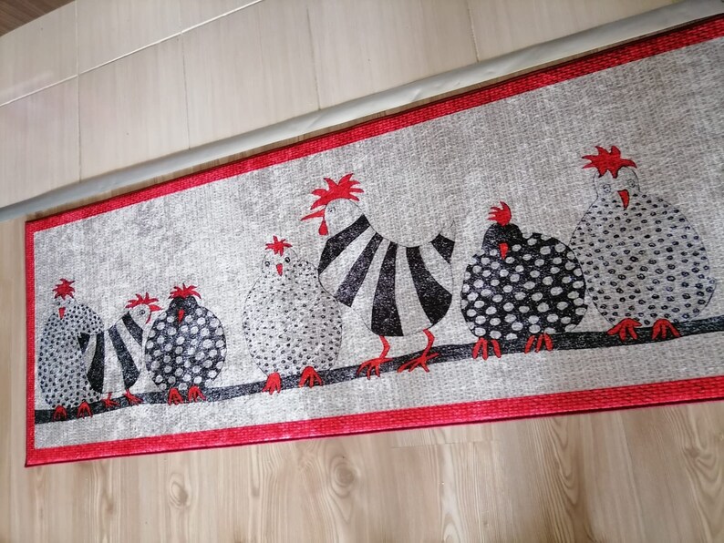 May include: A gray and white kitchen rug with a red border features a line of black and white chickens with red combs. The chickens are in a row, facing the right side of the rug.