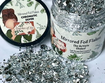 May include: A clear jar filled with silver mirrored foil flakes. The jar has a black lid with a label that reads "Mirrored Foil Flakes Chromatic Silver Touches of Su".