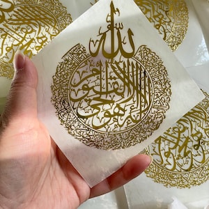 May include: Gold foil stickers with Arabic calligraphy. The stickers feature a circular design with the word "Allah" in the center. The stickers are on a white background.