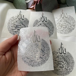 May include: Five silver stickers with Arabic calligraphy. The stickers are on white paper and feature a circular design with the word "Allah" in the center.