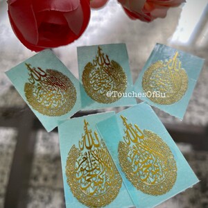 May include: Four gold-colored stickers with Arabic calligraphy on a light blue background. The stickers feature the word "Allah" in a decorative circle.