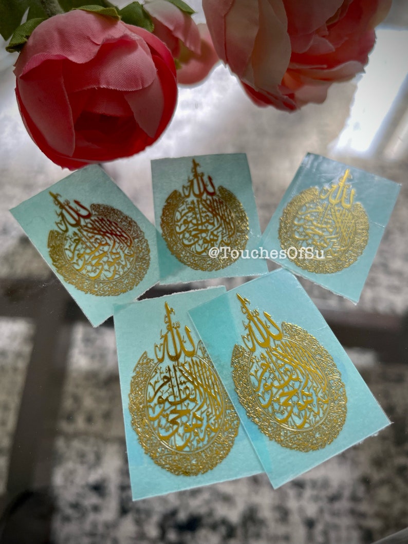 May include: Four gold-colored stickers with Arabic calligraphy on a light blue background. The stickers feature the word "Allah" in a decorative circle.