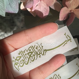 May include: Gold foil calligraphy on a white background with the Arabic phrase "Bismillah Al Rahman Al Rahim" which translates to "In the name of Allah, the Most Gracious, the Most Merciful".