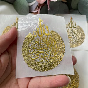 May include: Gold foil stickers with intricate Arabic calligraphy in a circular design. The stickers feature the word "Allah" in the center.