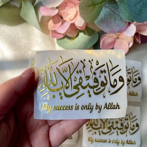 May include: Gold foil stickers with Arabic calligraphy and the English text "My success is only by Allah." The stickers are rectangular and feature ornate script. Several stickers are visible, with a soft floral background.