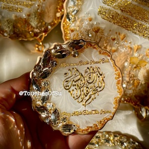 May include: Decorative resin coasters with gold accents and Arabic calligraphy. The coasters have a white base with gold leaf and crystal embellishments. The text "May Allah Bless This Home" is visible.