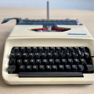 May include: A vintage white typewriter with a black keyboard and a blue label that says "Olivetti Lettera 32".