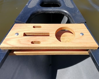 May include: A wooden canoe cup holder with a round cutout for a cup and three rectangular cutouts for other items. The holder is attached to the canoe with screws and has the text "MADE IN THE USA" engraved on the side.