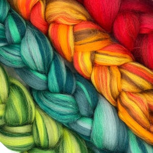 May include: Close-up of colorful fiber braids in shades of green, teal, orange, yellow, and red. The fiber is soft and fluffy, with a textured appearance. The braids are arranged in a diagonal pattern, creating a visually appealing design.