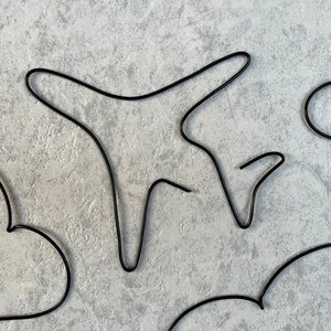 May include: Black wire shapes in the form of hearts and an aeroplane. The shapes are on a light grey background.