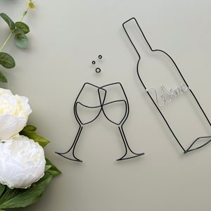 Może przedstawiać: Szklana rzeźba z drutu przedstawiająca dwa kieliszki do wina, kt&oacute;re się toastują, z butelką wina, na kt&oacute;rej napisano "Wine".