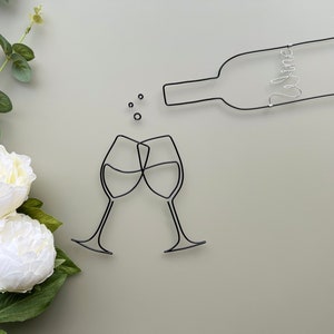 Może przedstawiać: Szklana rzeźba z dw&oacute;ch kieliszk&oacute;w do wina, kt&oacute;re się toastują, z butelką wina nad nimi. Butelka ma napis "wine".