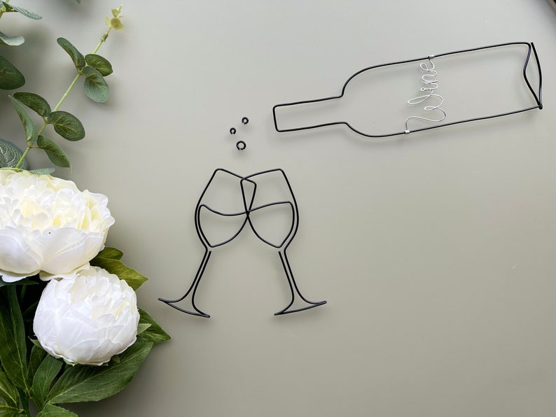 Może przedstawiać: Szklana rzeźba z dw&oacute;ch kieliszk&oacute;w do wina, kt&oacute;re się toastują, z butelką wina nad nimi. Butelka ma napis "wine".