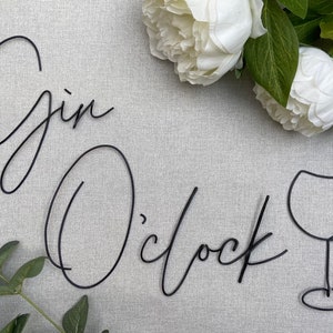 May include: Black metal wire wall art with the words "Gin O'clock" and a stylized image of a wine glass.