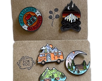 May include: Set of six enamel pins featuring outdoor adventure themes. The pins include a campfire, a van, a mountain scene, a moon and stars, a backpack, and a text design that says "Pack Lighter Go Further".
