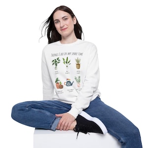 Puede incluir: Sudadera blanca con el texto "Things I do in my spare time" y un gráfico de plantas en maceta con texto que describe actividades relacionadas con las plantas.