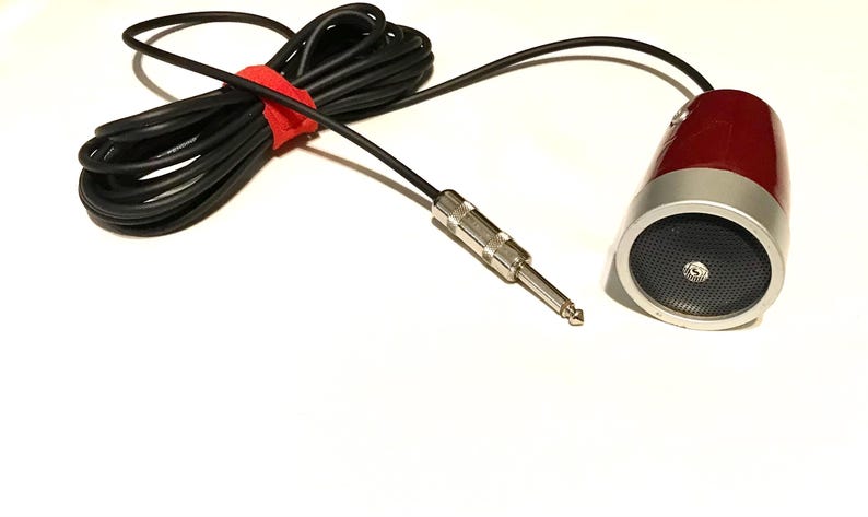 May include: A red and silver microphone with a black mesh grille and a long black cable. The cable features a silver-colored 1/4-inch jack plug and is secured with a small red hook-and-loop fastener strap to keep the cord neatly coiled.