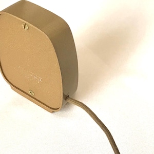 Puede incluir: Un dispositivo el&eacute;ctrico de color marr&oacute;n claro, de forma cuadrada con esquinas redondeadas y un acabado mate liso. El panel trasero est&aacute; asegurado con dos tornillos visibles y un cable el&eacute;ctrico fino de color marr&oacute;n claro sale del lado inferior derecho.