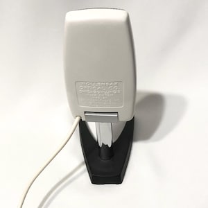 May include: A white Wollensak Optical Co. device with a chrome stand and black base. The white casing features embossed text: WOLLENSAK OPTICAL CO. CHICAGO-ILLINOIS MODEL 8H32-A MFD BY REVERE CAMERA CO. MADE IN U.S.A. A white power cord extends from the side.