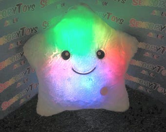 Peut inclure: Un coussin en forme d'étoile blanc en peluche avec un visage souriant et une fonction d'éclairage qui change de couleur. Le coussin est éclairé par un arc-en-ciel de couleurs, y compris le rouge, l'orange, le jaune, le vert, le bleu, l'indigo et le violet.