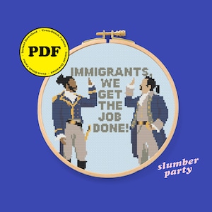 Può includere: Schema di punto croce con due uomini in abiti d'epoca coloniale, uno nero e uno bianco, con il testo "Immigrants, We Get The Job Done!" Lo schema è in un cerchio blu chiaro con una cornice in legno. Il testo "slumber party" è scritto sotto il cerchio.