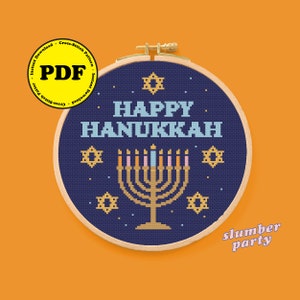 May include: A blue cross-stitch pattern with a menorah and the text "Happy Hanukkah". The pattern is in a wooden embroidery hoop.