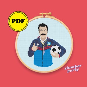 Peut inclure: Un motif de point de croix représentant un dessin animé d'un homme avec une moustache portant un survêtement bleu et rouge et tenant un ballon de football. Le motif est dans un cerceau de broderie en bois et le texte "slumber party" est sous le cerceau.
