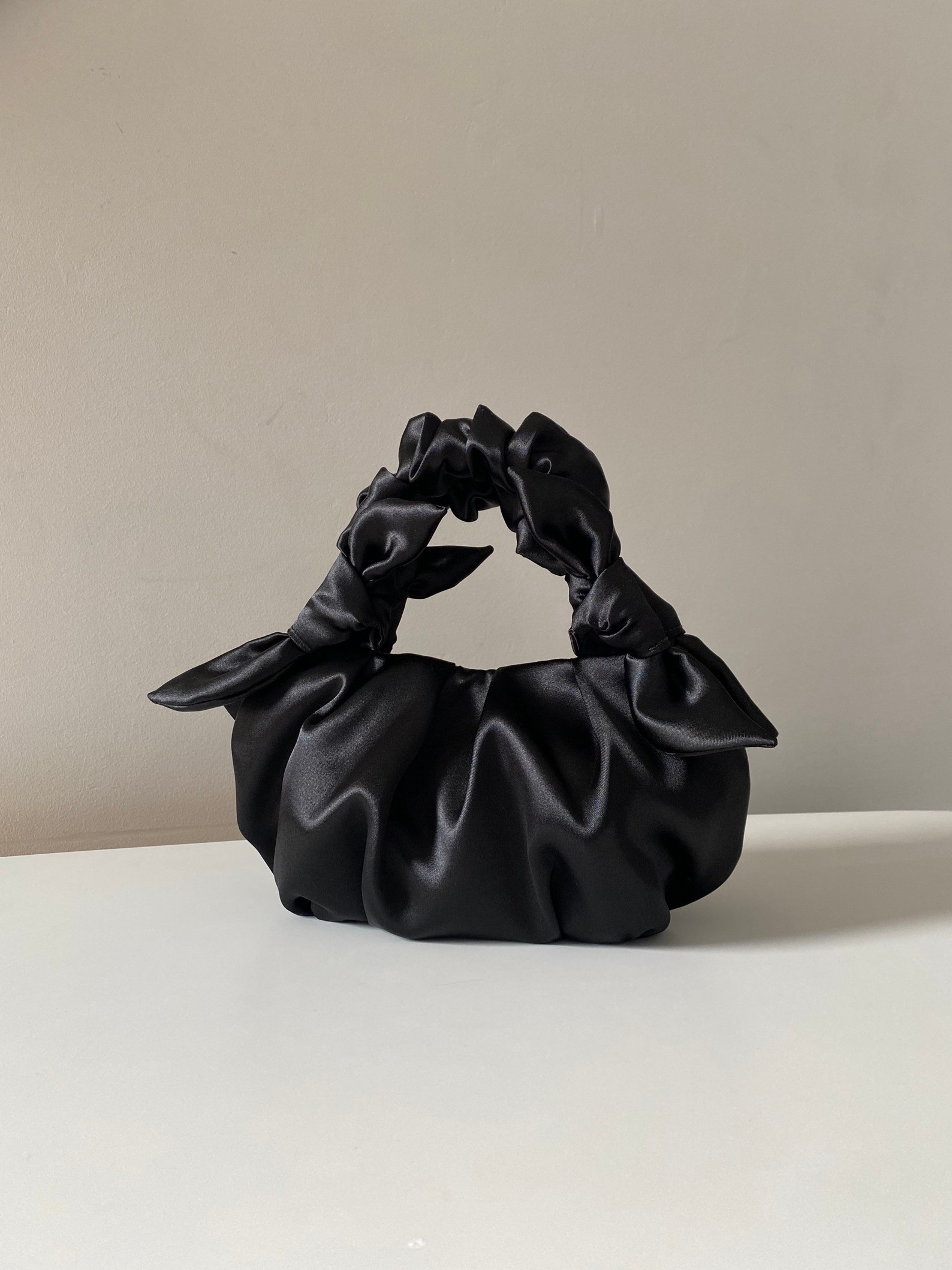Black evening bag with knots crafted from smooth satin. Beautiful designer woman bag is soft, but keeps its shape, closes with a magnetic button. Stylish black satin bag is made in vintage style, based on the Japanese technigue of tying a silk scarf in a bag. Small satin bag is able to decorate not only official event, but also becomes a companion for every day. Perfect wedding bag.