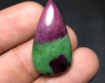 May include: A polished, teardrop-shaped gemstone featuring a vibrant color combination. The top portion is a deep, rich magenta, transitioning to a band of bright green, and ending with a patch of magenta at the base. The stone has a smooth, reflective surface.