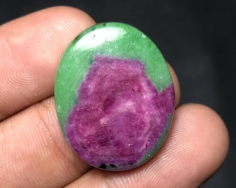 May include: Oval-shaped gemstone with a vibrant color combination. The stone features a rich, deep magenta center surrounded by a bright green border. The polished surface reflects light, highlighting the natural patterns and textures of the stone.