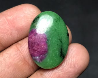 May include: Oval-shaped gemstone with a vibrant green base and a prominent magenta-colored inclusion. The polished surface reflects light, showcasing the stone's natural patterns and textures. The gemstone is a natural mineral.