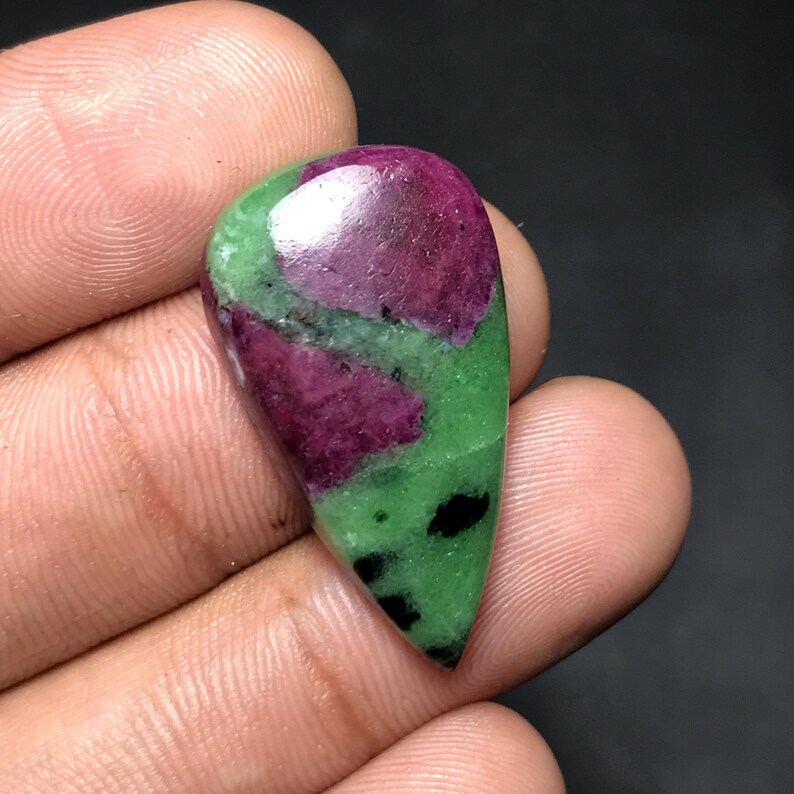 May include: A polished, teardrop-shaped gemstone featuring a vibrant mix of colors. The stone showcases a deep burgundy hue at the top, transitioning to green with dark spots, creating a striking contrast. This gemstone is ideal for jewelry.