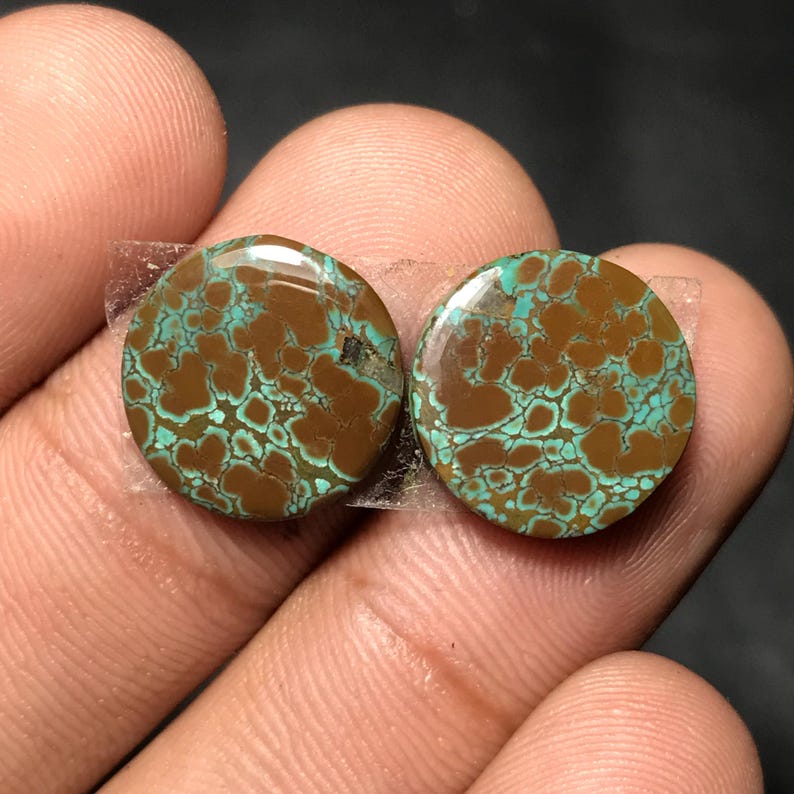 Op de afbeelding: Twee ronde, gepolijste edelstenen. Elke steen heeft een bruine basiskleur met een turquoise, webachtig patroon. De stenen worden bij elkaar gehouden met doorzichtige tape, wat hun natuurlijke schoonheid en unieke ontwerp benadrukt.