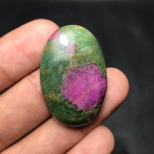 May include: An oval gemstone displaying a striking contrast of colours. The stone has a central area of deep pink, encircled by a mottled green. The polished surface catches the light, accentuating the natural patterns and textures.
