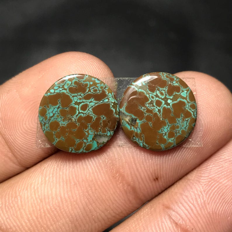 Op de afbeelding: Twee ronde, gepolijste edelstenen met een bruin en turquoise patroon. De stenen worden bij elkaar gehouden met doorzichtige tape. De edelstenen hebben een unieke, natuurlijke uitstraling, met een netwerk van turquoise aderen tegen een bruine achtergrond.